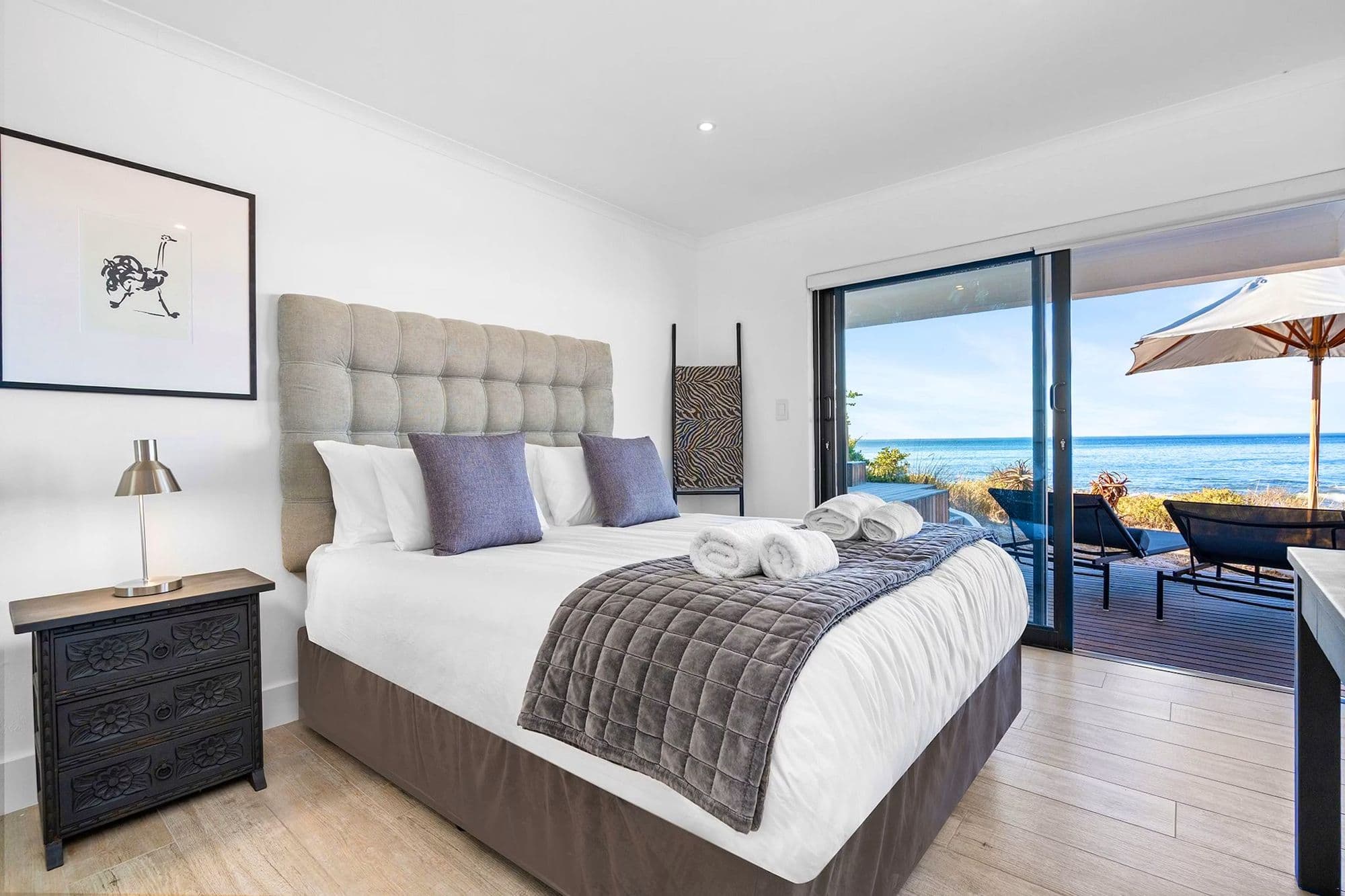 A sea-facing bedroom with sliding doors onto a private balcony with an umbrella and loungers