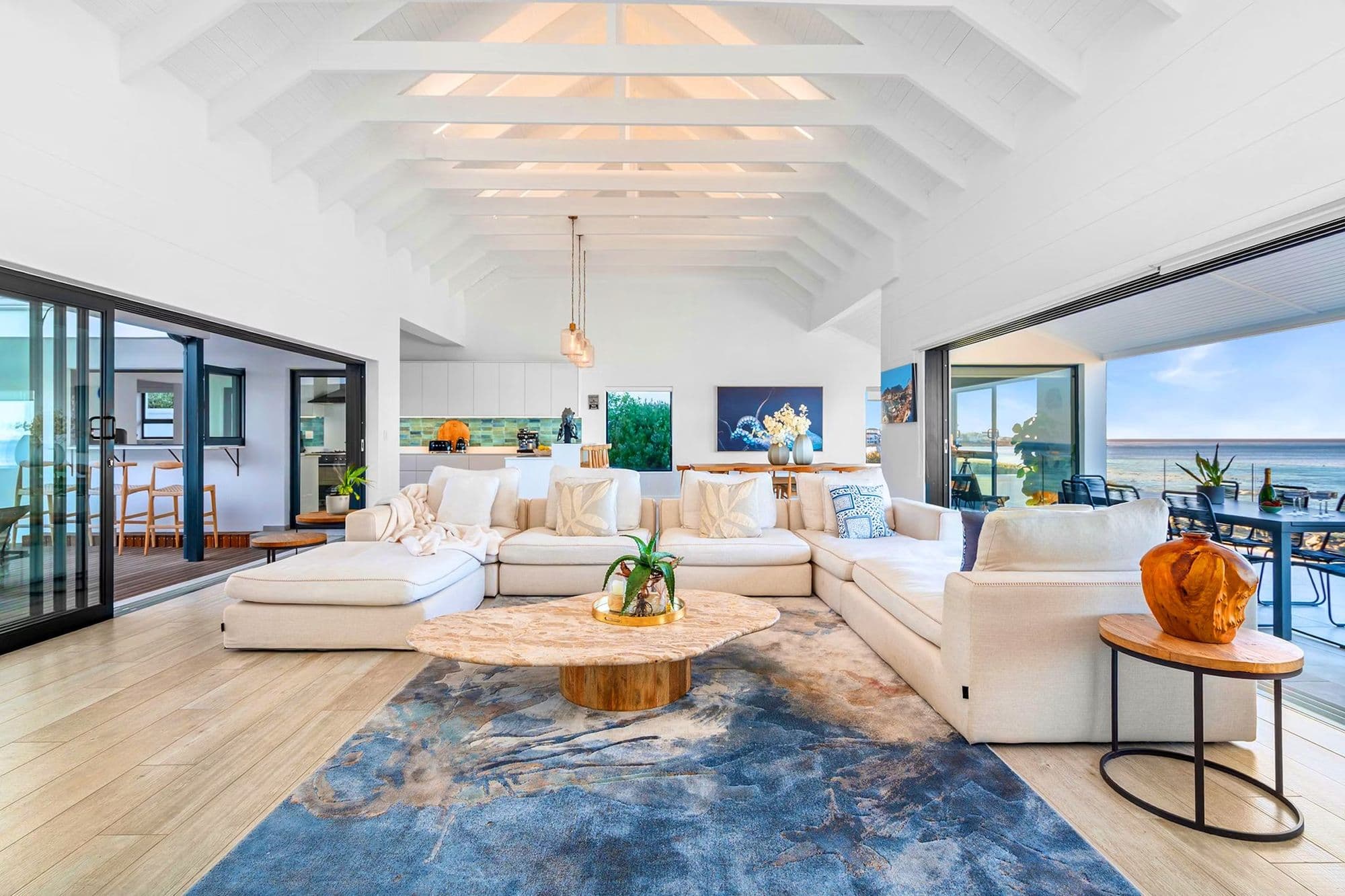 An open-plan living room with vaulted timber ceilings and glass walls to the sea